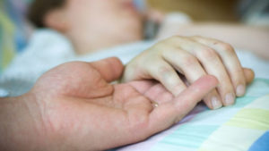 A person holding the hand of someone on a hospital bed