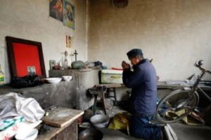 A Chinese man praying to a cross in his home