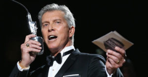 A man in a tuxedo singing into an old-style microphone